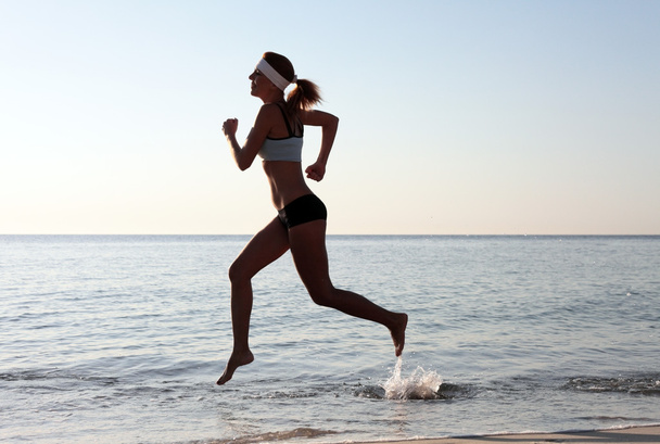 Красива молода спортивна жінка біжить на пляжі
. - Фото, зображення