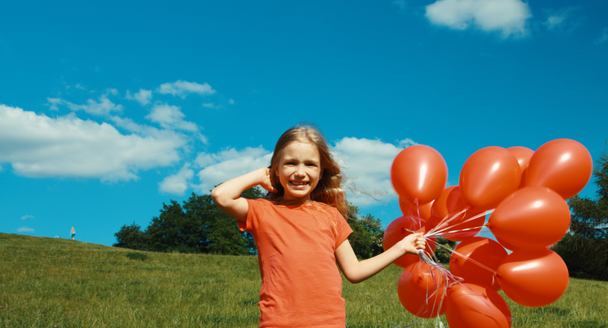Portrait girl with red balloons walking in the meadow - Záběry, video