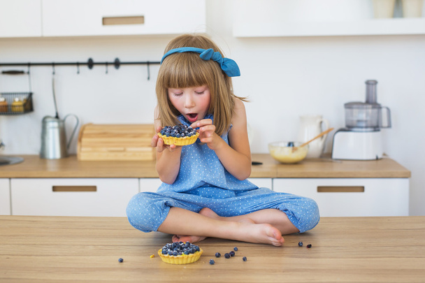 Cute little girl in blue dress eats a cakes on a table - Foto, Imagem