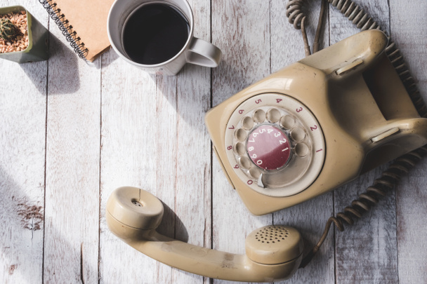 Widok z góry na stary telefon z filiżanką kawy, notebookiem i kaktusem na białym drewnianym tle stołu. - Zdjęcie, obraz