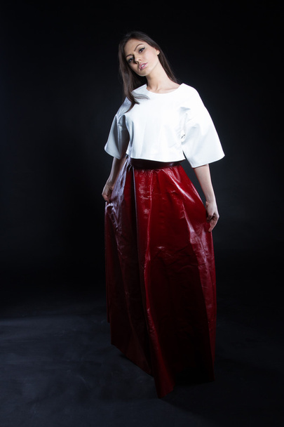 白いブラウスと黒の背景に赤のロング スカートの美しい少女。スタジオ ポートレート. - 写真・画像