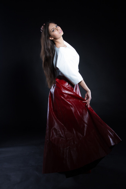 Beautiful young girl in a white blouse and a long skirt red on a black background. Studio portrait. - Foto, imagen