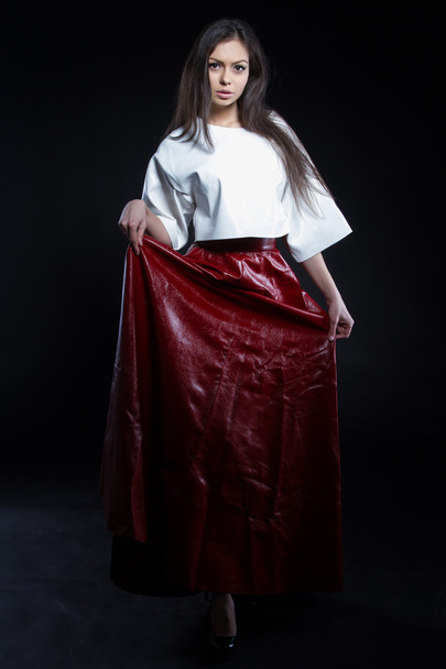 Beautiful young girl in a white blouse and a long skirt red on a black background. Studio portrait. - Foto, afbeelding