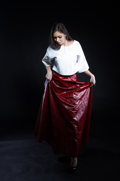 Bella ragazza in una camicetta bianca e una gonna lunga rossa su uno sfondo nero. Ritratto studio
. - Foto, immagini