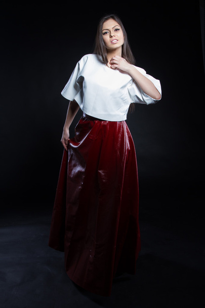 Piękna młoda dziewczyna w białej bluzce i czerwoną długą spódnicę na czarnym tle. Portret Studio. - Zdjęcie, obraz