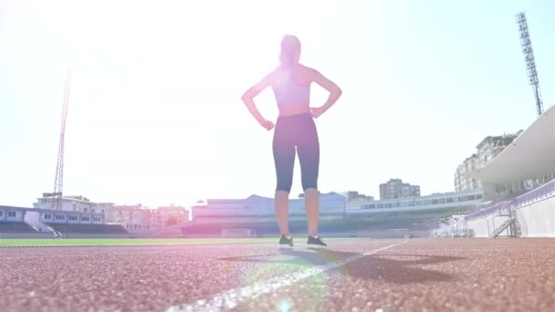 Track runner athlete woman warming up before running at a stadium, sun flare - 映像、動画