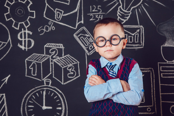 Kleine jongen als zakenman of leraar met bril staande haar handen gevouwen op een donkere achtergrond patroon - Foto, afbeelding