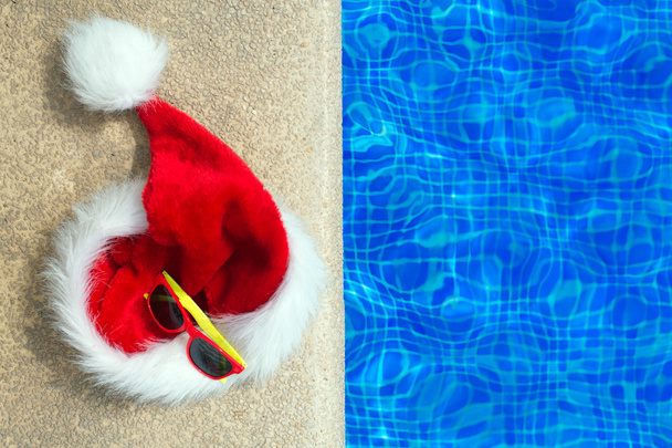 Piros karácsonyi kalap és napszemüveg közelében a medence. Hely a szöveg. - Fotó, kép