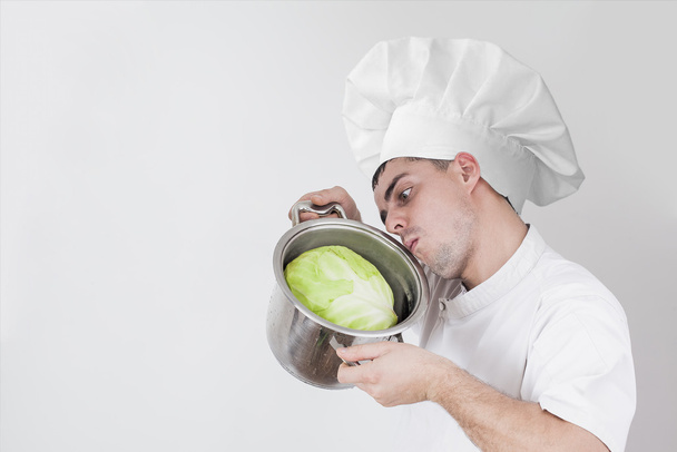 young man in white uniform holding pot with  cabbage against gray texture background - Foto, immagini