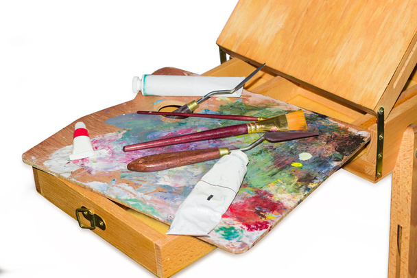 Ferramenta de pintura na paleta em um fecho de cavalete de madeira
 - Foto, Imagem