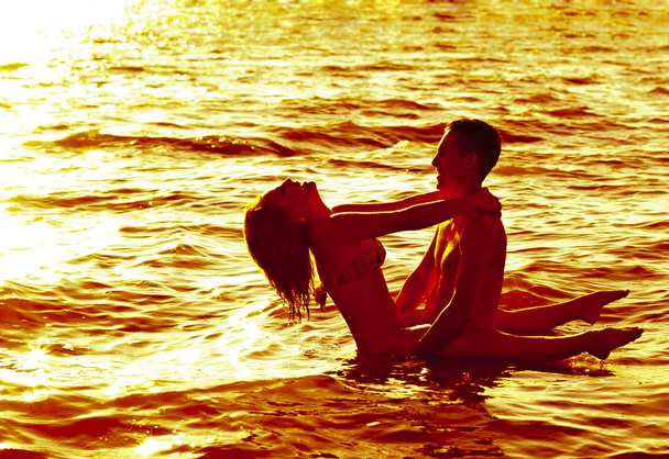 Two young adult lovers standing in water at  sunset  - Photo, Image