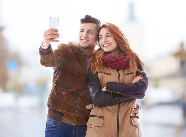 Young happy couple taking selfie on blurred city street background - 写真・画像