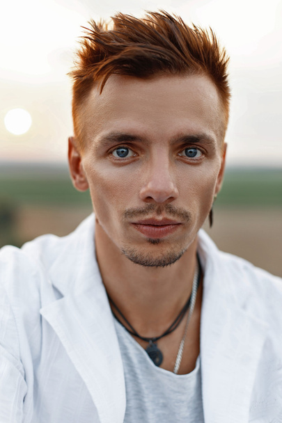 Portret van een jonge knappe man in een wit pak bij zonsondergang - Foto, afbeelding