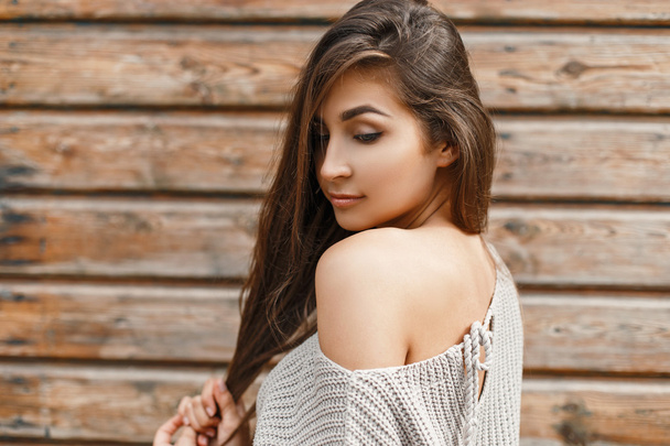 Красива молода жінка в сірому светрі біля старовинної дерев'яної стіни
 - Фото, зображення