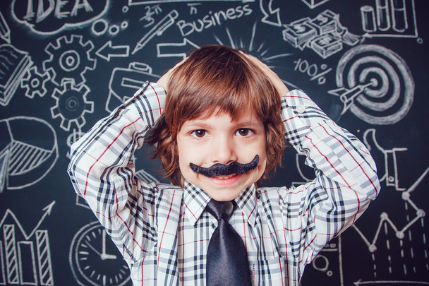 Little boy as businessman or teacher with mustache standing on dark background pattern. Wearing shirt and tie. He keeps holding his head. close-up - Photo, Image