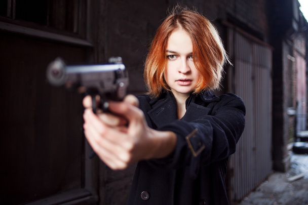 Woman pointing a gun. Mafia girl shooting at someone on the street. Emotion of fear, fright - Foto, immagini