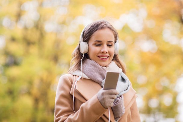 woman with smartphone and earphones in autumn park - 写真・画像