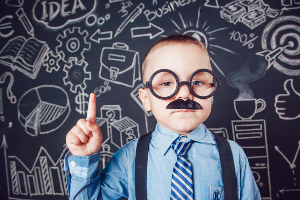 Little boy as businessman or teacher with mustache and glasses standing on dark background pattern. Wearing shirt, tie. Lifting a finger up - Photo, Image
