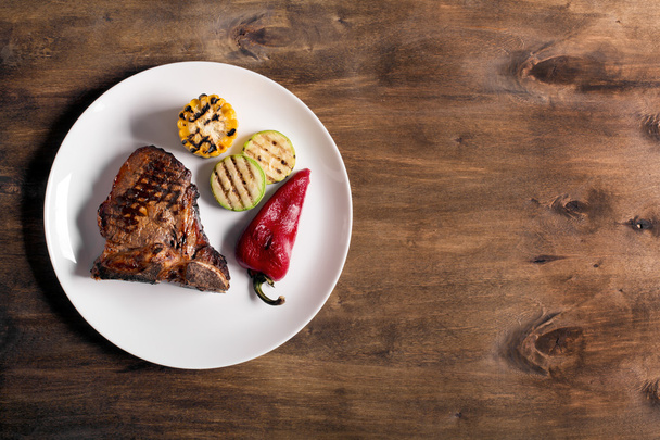 Grilled steak on brown wooden background with vegetables - Foto, imagen
