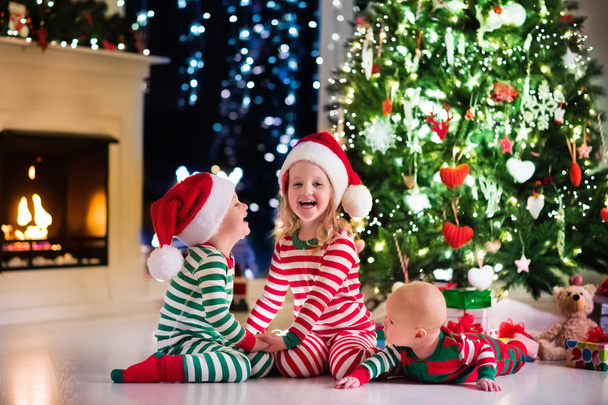 クリスマス ツリーの下のパジャマを着て子供たち - 写真・画像