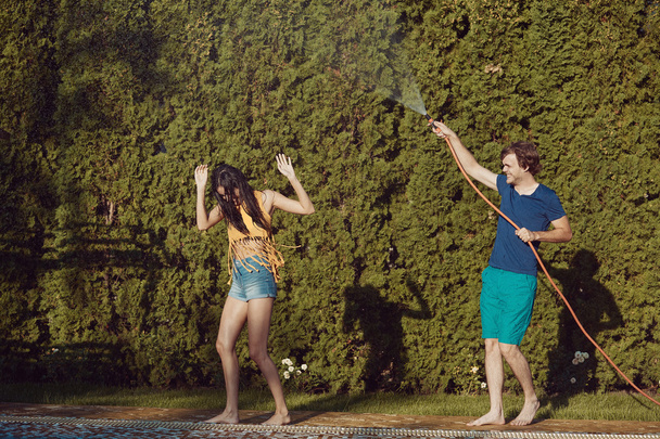Couple having fun pour each other with garden hose - Фото, зображення