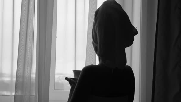 Seductive girl dressed in towel with neat body is holding a cup with hot tea or coffee, standing near the window in her home or hotel room - Metraje, vídeo