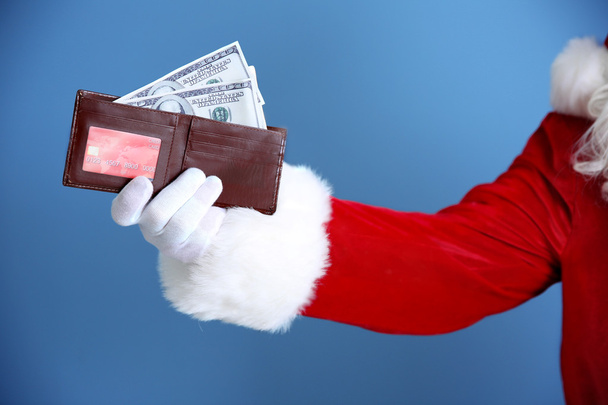 Santa Claus hand holding wallet with money and credit card on blue background - Fotoğraf, Görsel