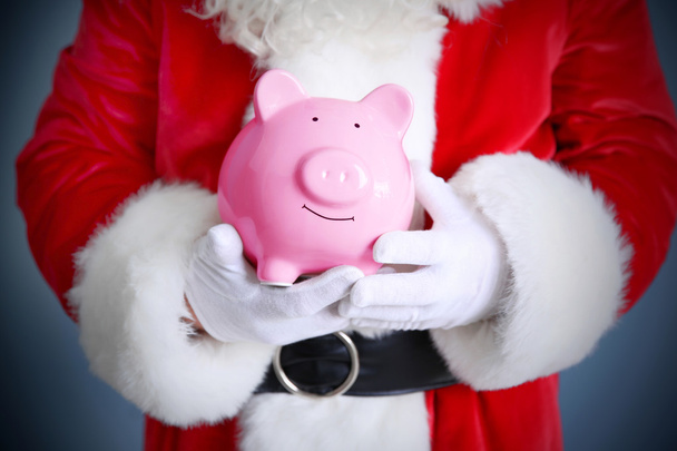 Santa Claus hands holding piggy bank on blue background - Foto, afbeelding