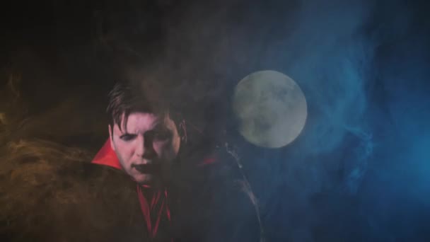 vampiro de Halloween usando capa negra y señalando su dedo sobre el fondo oscuro de la luna ahumada
 - Metraje, vídeo