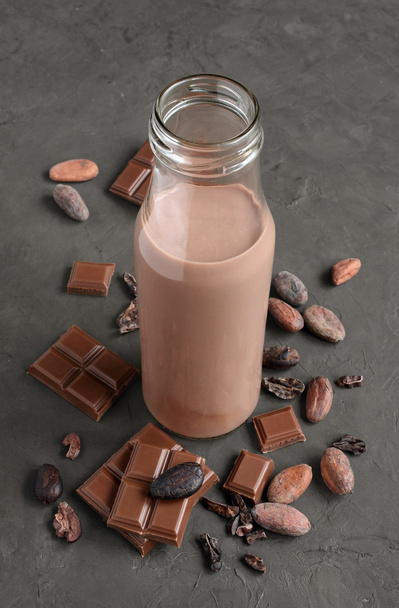 Leite de chocolate em uma garrafa de vidro com pedaços de barra de chocolate e feijão de cacau
 - Foto, Imagem