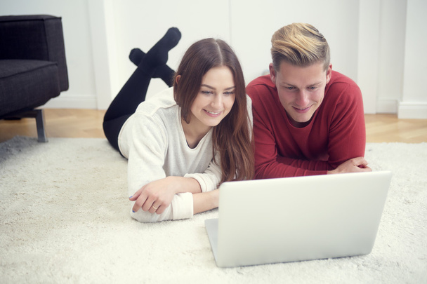 若いカップルは、床に横になっていると、コンピューターを見て - 写真・画像