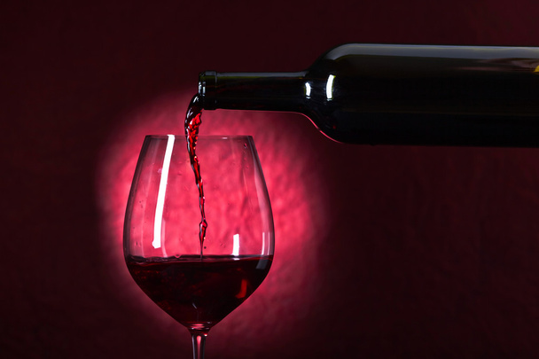 Fles en glas rode wijn op een donkere achtergrond - Foto, afbeelding