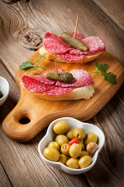 Tapas with sliced salami, olives and cucumber on a wooden table. - Foto, Bild