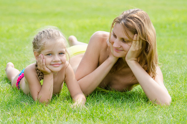 Young mother lying on green grass and looking at his five-year daughter who is lying near - Photo, image