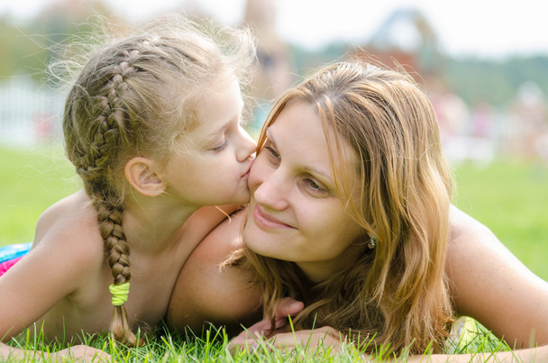 緑の草の芝生の上で横になっている彼女の母親にキス 5 年の娘 - 写真・画像
