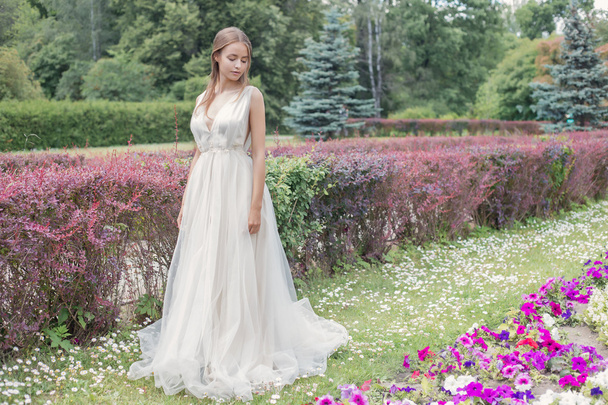 Beautiful tender young woman bride in her wedding dress gentle air walks in the lush garden on a hot sunny summer day - Foto, Bild