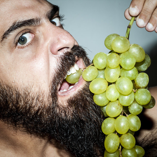 Mann mit Bart, der unersättlich Trauben isst - Foto, Bild