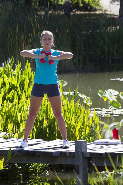 young woman training with dumbbells on wooden bridge and water - Foto, afbeelding