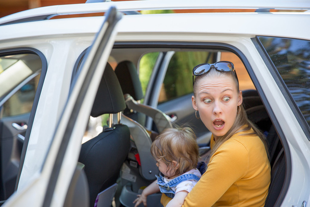 Mujer joven con mirada sorprendida salir del coche con el bebé
 - Foto, Imagen