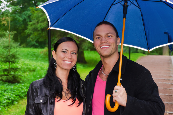 Portrait of young couple under umbrella in the park - Фото, изображение