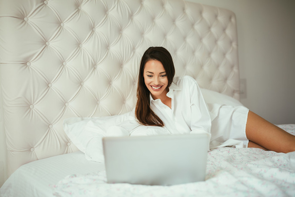 Beatufiul brunette using laptop in bed - Foto, afbeelding