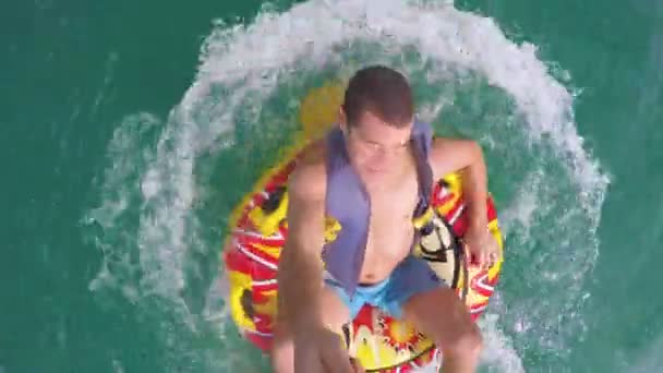 Człowiek siedzi w nadmuchiwany pierścień ciągniętym przez łódź w wodzie i nagrywania siebie aparatem Go Pro - Materiał filmowy, wideo