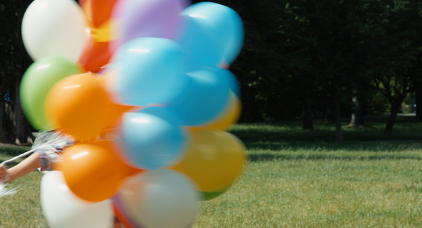 Portrait girl spinning with balloons in the meadow at camera and waving hand at camera - Footage, Video