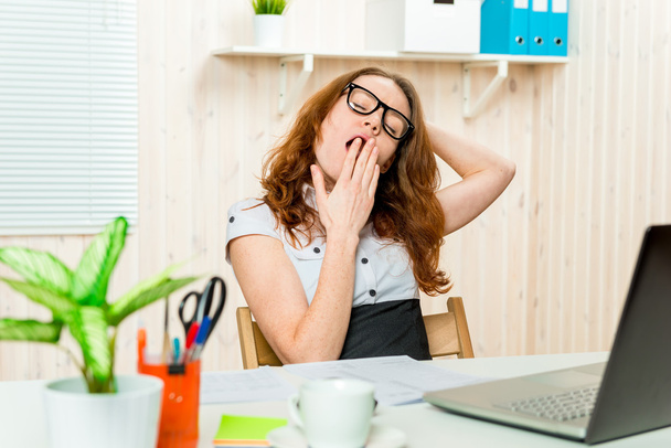Втомлена бізнес-леді позіхання і розтягування за його столом в
 - Фото, зображення