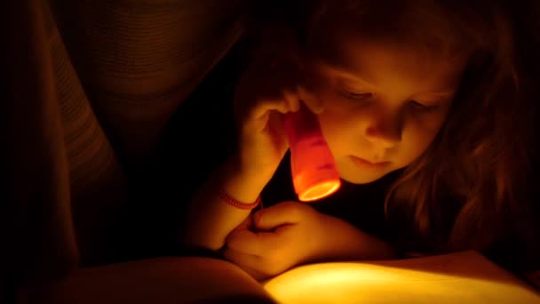 Lány olvasó a zseblámpával takaró alatt. Gyermek olvasatban az ágyban. Közelről kislány olvasó egy könyv az ágyban - Felvétel, videó