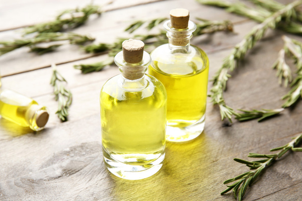 Bottles of coniferous essential oil and rosemary branches on wooden background, close up view - Фото, зображення