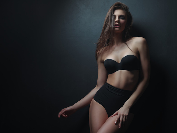 Seductive, beautiful and attractive young woman with loose brown hair and sexy gorgeous figure in the black seamless underwear and wool coat on the naked body is posing in the studio - Φωτογραφία, εικόνα