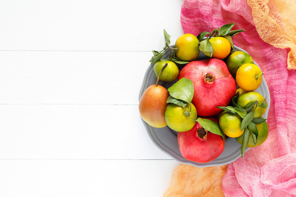 ピンクの繊維と白い木製の背景の水平方向の画像上の果物ザクロ、ミカン、梨の美しいセット - 写真・画像