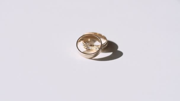 Rotation von zwei goldenen Ringen mit Diamanten auf einer weißen Oberfläche - Filmmaterial, Video