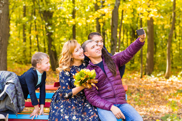 familia, temporada, tecnología y concepto de personas - familia feliz tomando selfie por teléfono inteligente en el parque otoñal
 - Foto, Imagen
